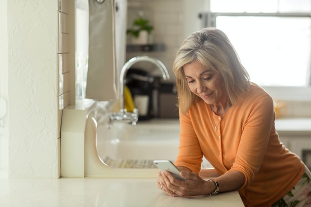 Woman shopping for prescriptions with online pharmacy on her phone in her kitchen